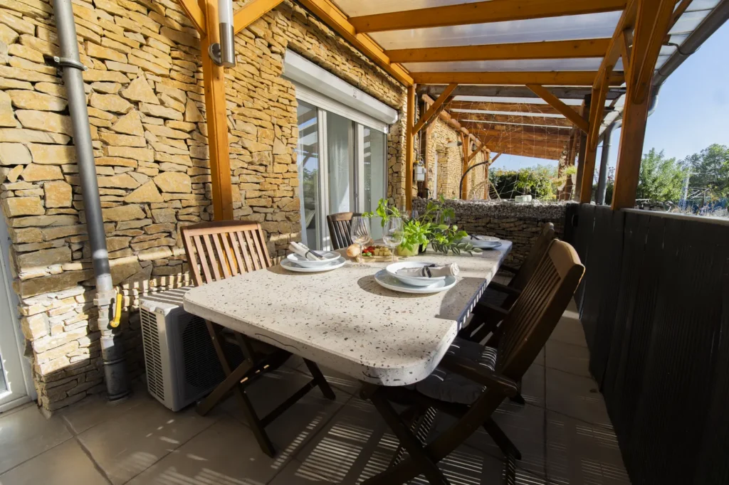 A terasz másik vége: kőfal, terített asztal és fa székek a pergola alatt